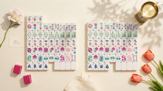 Four women compare mahjong tiles by weight at a community center table, racks and mat in front of them