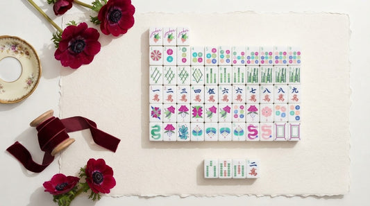 Four women playing mahjong in a bookstore cafe nook with a wrapped gift box on a side table