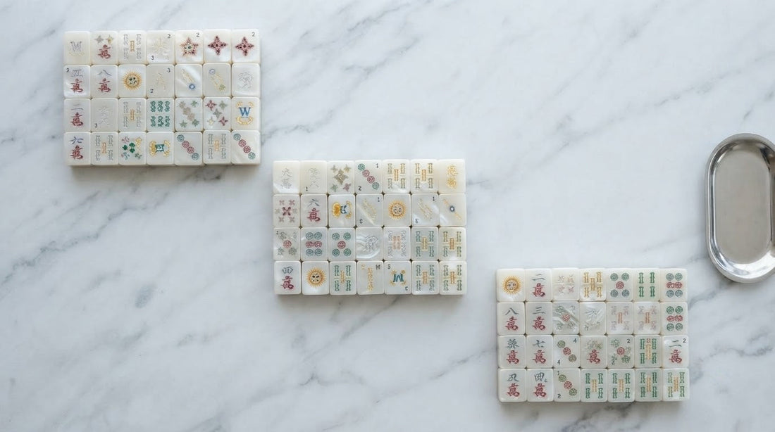 Woman tilting a clear glossy tile to the light at a mahjong table in a sunlit studio loft