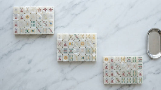 Woman tilting a clear glossy tile to the light at a mahjong table in a sunlit studio loft