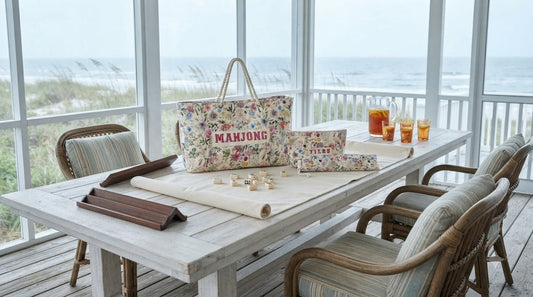 Four women playing mahjong on a breezy beach house sunporch beside an open coastal window
