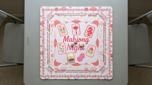 Four women playing a quiet mahjong round on a thick non-slip mat in a book-lined library room
