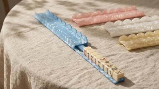 Four women sliding ivory tiles across mahjong racks fitted with pushers at a bright game room table
