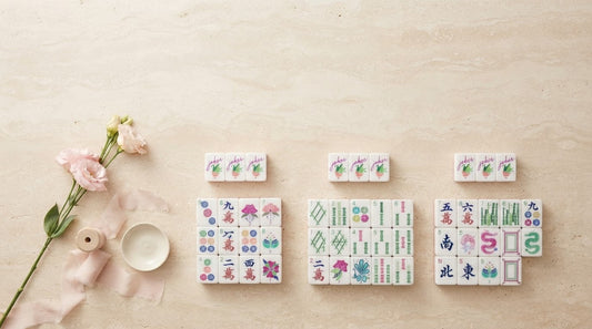 Four women admiring a pastel-toned mahjong set at a table in a bright apartment party room