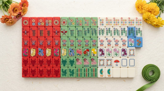 Four women in a salon lounge holding up a vivid pink mahjong tile above racks of ivory tiles