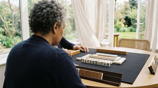 Library meeting room table where one player studies a rival's exposed tiles with narrowed eyes
