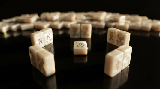 Four women at a library table as one claims a discarded mahjong tile from the mat