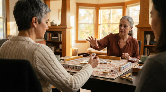 Four women playing at a library meeting room table, one setting a drawn tile onto her rack