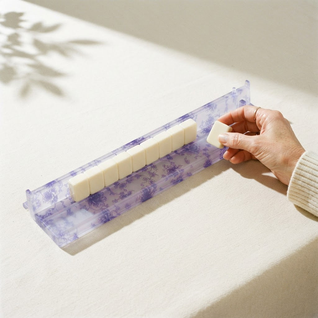 A hand laying a tile on a Blue Toile mahjong rack lined with ivory tiles