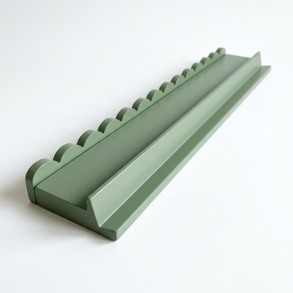 A sage green mahjong rack with a scalloped pusher on a white background