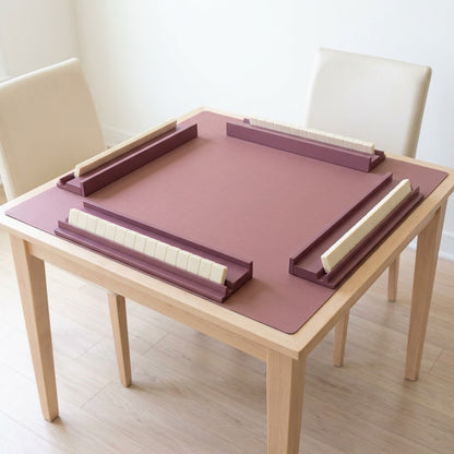 Four dusty rose mahjong racks on a matching mat on a light wood table