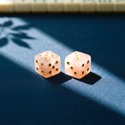 Two rose quartz mahjong dice with gold pips on a navy mahjong mat