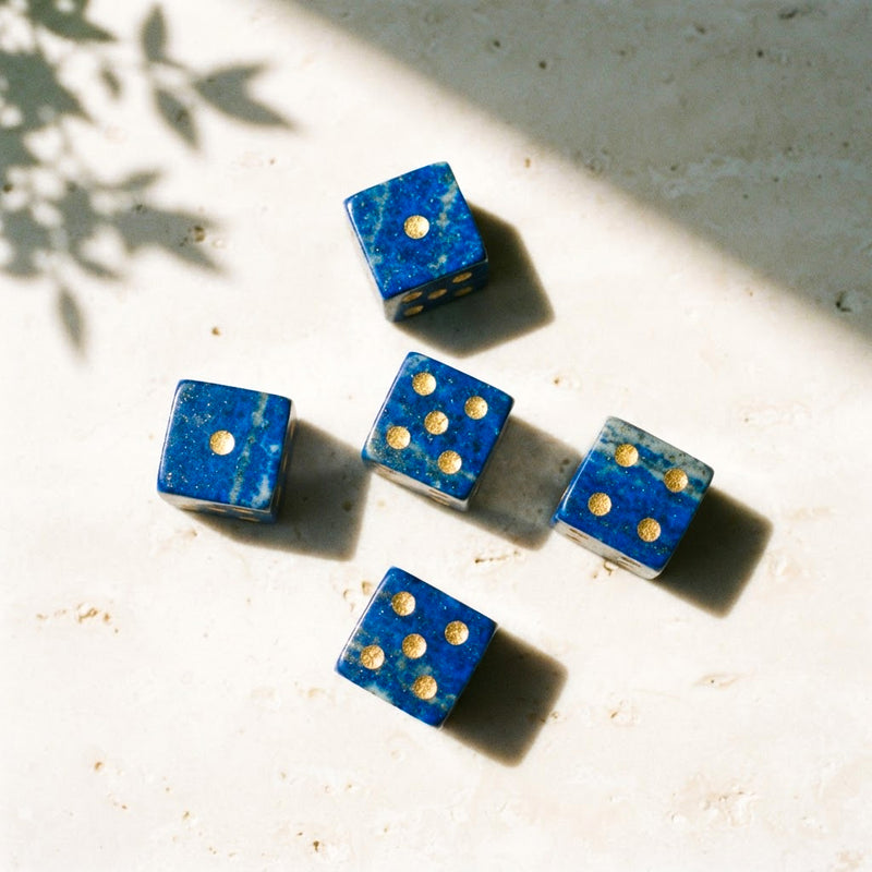 Lapis lazuli mahjong dice with gold pips scattered on pale travertine