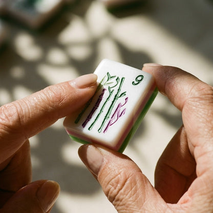 Fingertips holding a bamboo tile, engraved artwork clearly visible