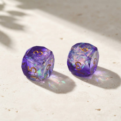 Two purple iridescent mahjong dice on a pale travertine table