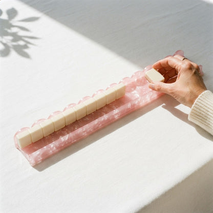 A hand setting a tile onto the shelf of a pink Pearl Shell mahjong rack