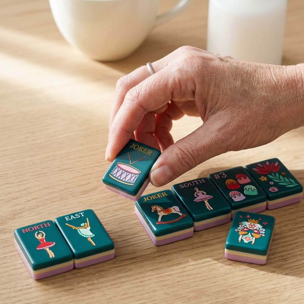 A hand setting a Sugarplum tile down onto the table beside a run of tiles already laid out