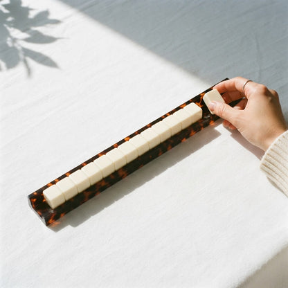 A hand laying a tile on a Tortoise Shell mahjong rack lined with ivory tiles
